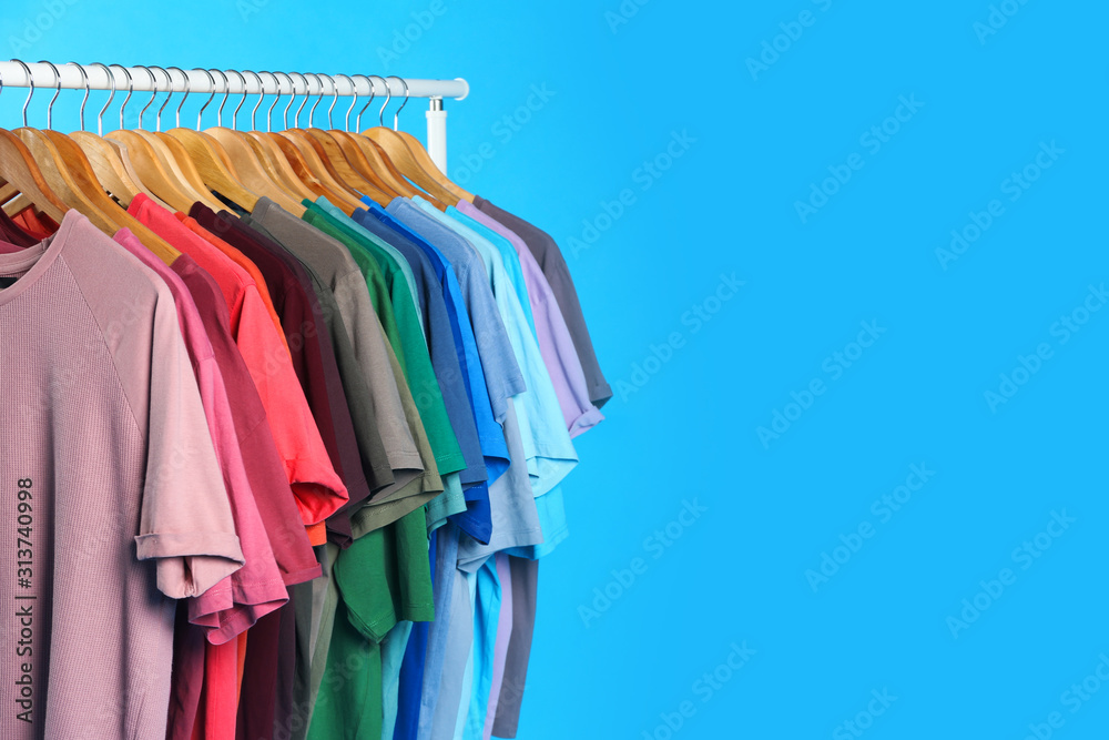 Colorful clothes hanging on rack against light blue background. Space for text