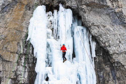 Ice Climbing Canada. Woman Ice Climber with crampons and axe in red jacket climbing Ice waterfall in Grotto Canyon, Canmore, Alberta Canada photo