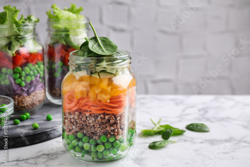 Healthy salads in glass jars on marble table. Space for text