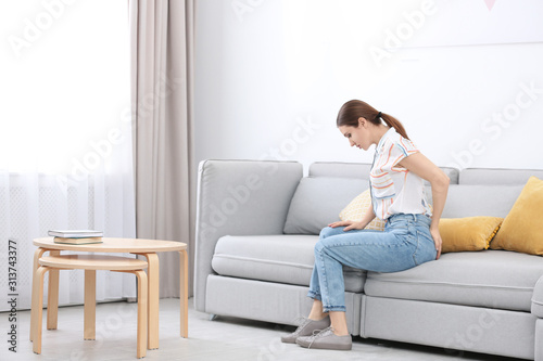 Young woman suffering from hemorrhoid on sofa at home