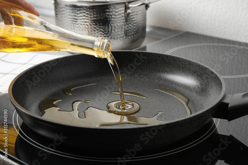 Woman pouring cooking oil from bottle into frying pan, closeup photo