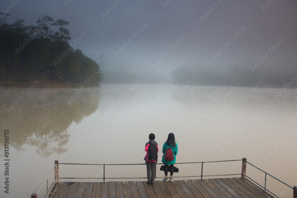 2 girls are standing on a foggy lake in a morning