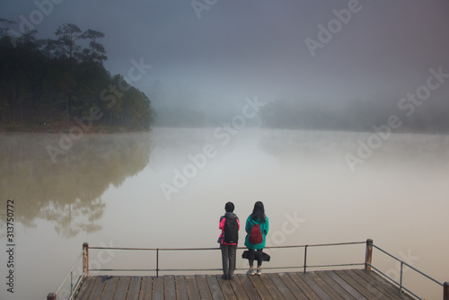 2 girls are standing on a foggy lake in a morning