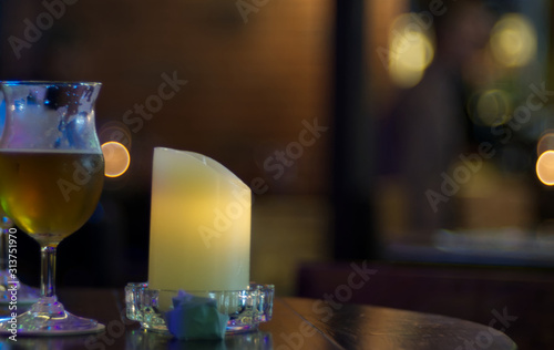 A candle and beer glas on a wooden desk with bubble blur background