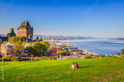 Cityscape view of Old Quebec City with buildings, green grass against St Lawrence river and blue sky in summer evening