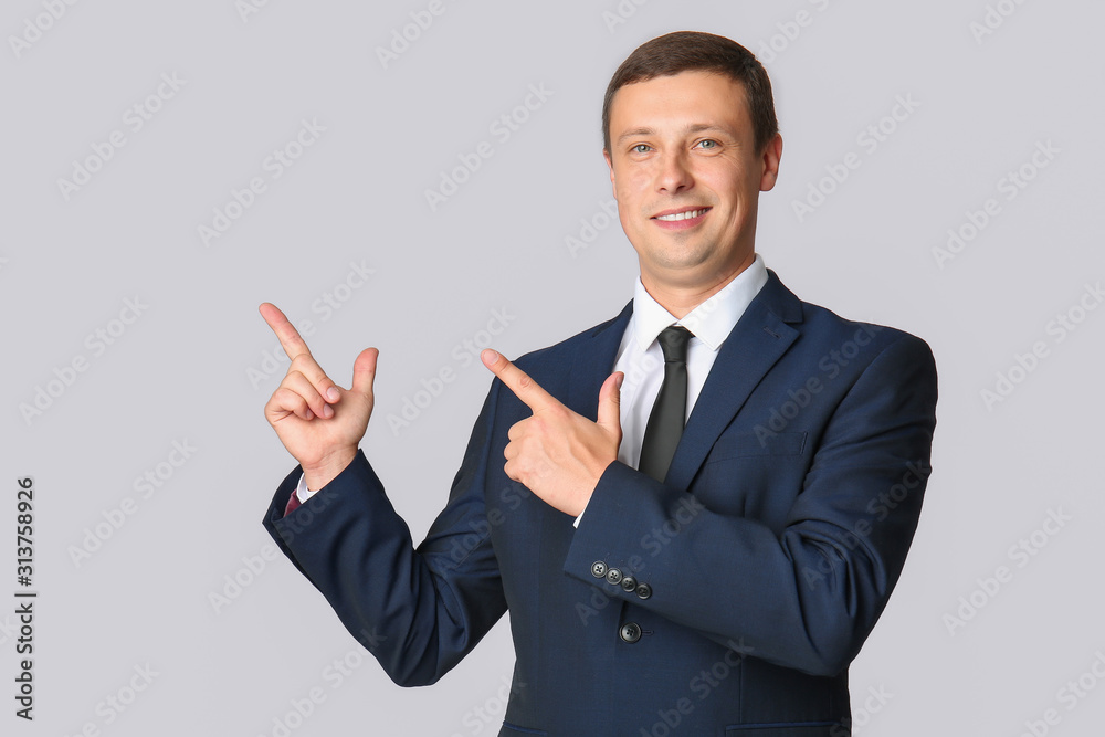 Portrait of handsome businessman pointing at something on grey background Portrait of handsome businessman pointing at something on grey background