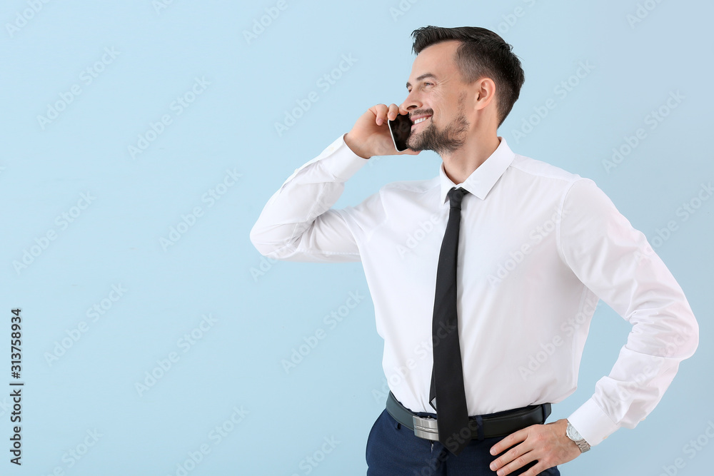 Portrait of young businessman talking by mobile phone on color background