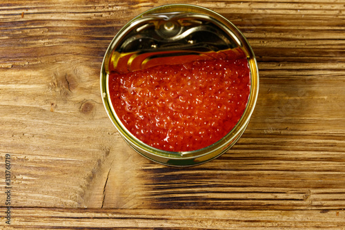 Open tin can with red caviar on wooden table. Top view