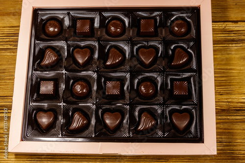 Assorted chocolate candies in a box on wooden table. Top view