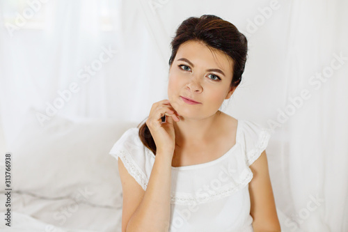 Young woman weared in white dress from natural fabric sits in wooden scandinavian interior. Relax and dream in white room Romantic girl in eco style interior. Natural materials concept