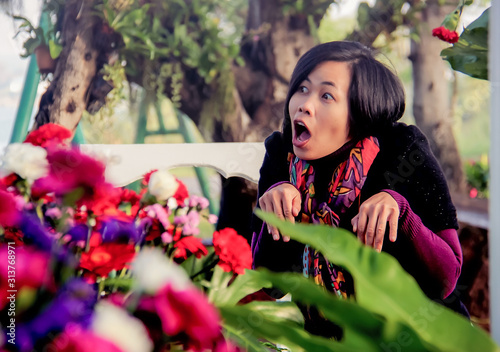 Asian woman standing in flower garden , making funny face,