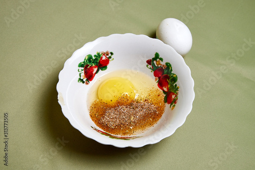 Fotografia Raw egg on a white plate on the table. Cooking eggs for cooking