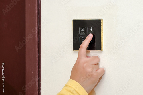 An asian woman hand finger try to push MAKE UP ROOM   switch at the  cream cement wall.