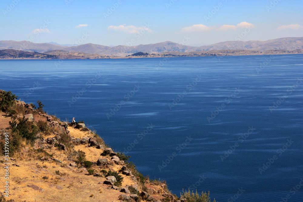 A Knitting Man sitting on the Edge of the Cliffs on Taquile Island overlooking Lake Titicaca towards Bolivia
