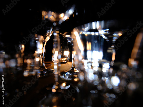 Close ups of wine-, long drink- and spirits-glasses on a wooden shelve in a bar, in front of a dark background, illuminated by colorful spot lights, creating blurry light effects with beautiful  bokeh