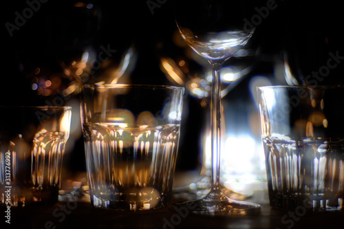 Close ups of wine-, long drink- and spirits-glasses on a wooden shelve in a bar, in front of a dark background, illuminated by colorful spot lights, creating blurry light effects with beautiful bokeh