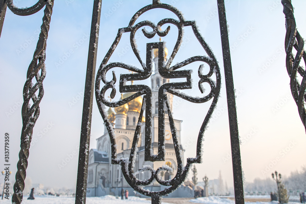 View of a church with golden domes through a forged fence in the shape of a church cross View of a church with golden domes through a forged fence in the shape of a church cross