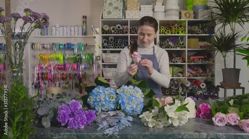 Cute Mature woman florist collects a bouquet and looks at the flowers with tenderness.