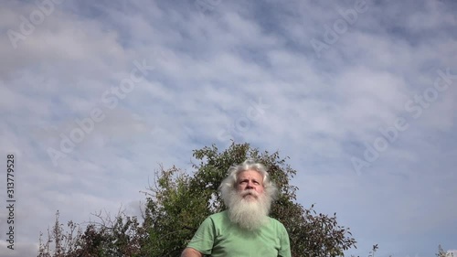 Sportive senior Caucasian man with splendid grey hair and beard is playing badminton. Beautiful portrait of active handsome European people in summer leisure. Outdoor lifestyle scene in slow motion