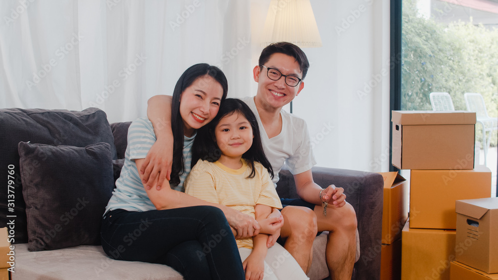 Happy Asian young family homeowners bought new house. Japanese Mom, Dad, and daughter embracing looking forward to future in new home after moving in relocation sitting on sofa with boxes together. Happy Asian young family homeowners bought new house. Japanese Mom, Dad, and daughter embracing looking forward to future in new home after moving in relocation sitting on sofa with boxes together.