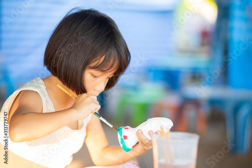 Little Asian girl painting plaster doll