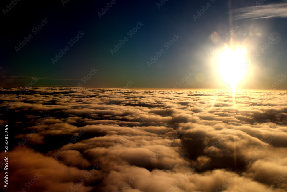 spectacular sunset seen from an airplane with clouds in the foreground,  blue sky and the sun in the distance