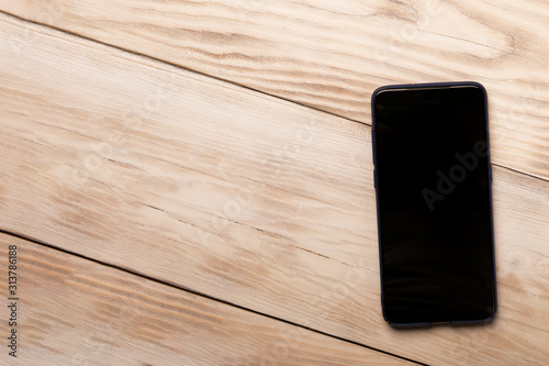 Mobile phone iphon style mockup with black screen on wooden background. Copy space