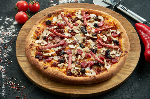 Pizza with a large number of toppings: hunting sausages, onions, mushrooms, salami, cheese and bell pepper. Pizza in composition with ingredients on a black background