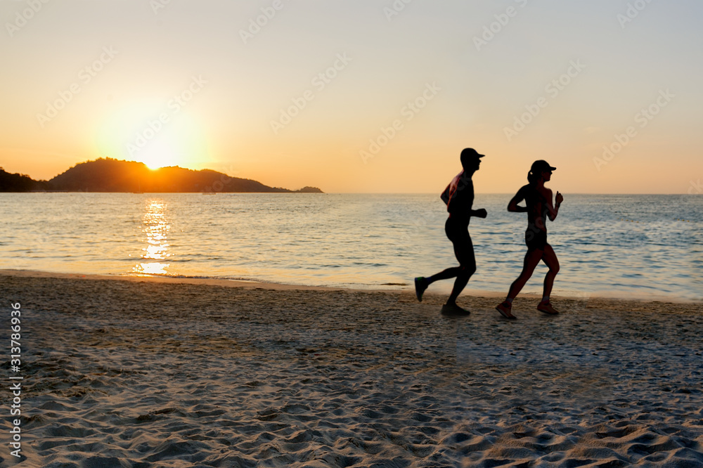 Silhouette of two sportive runners running on the beach at sunset. Man and women running on tropical beach.