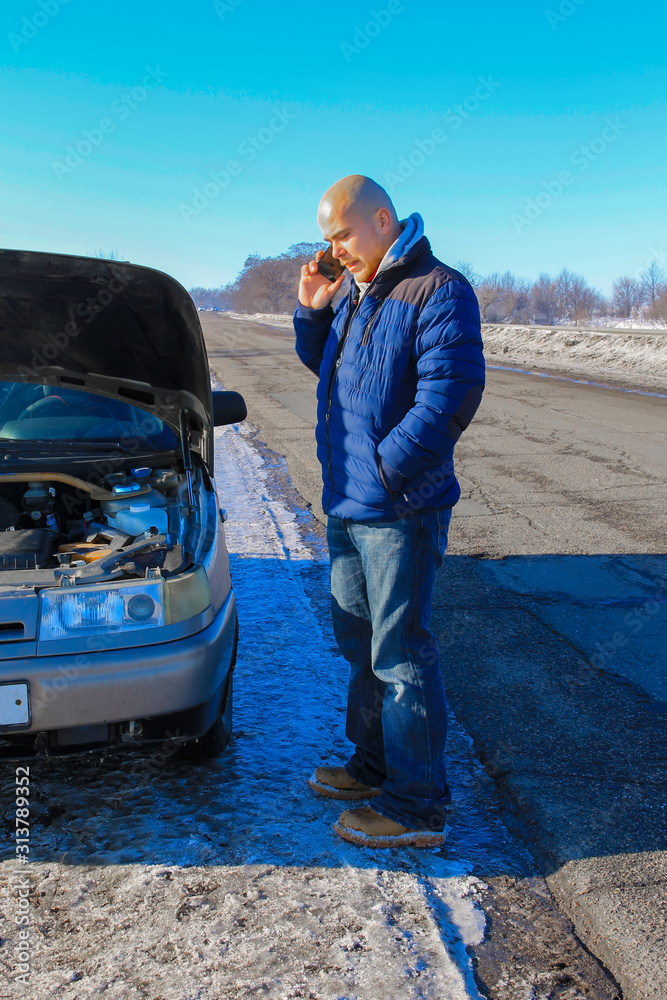 Upset young man calling the car service standing near a broken car at winter road Upset young man calling the car service standing near a broken car at winter road