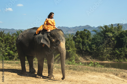 Photography Woman wearing beautiful orange dress is riding the elephant