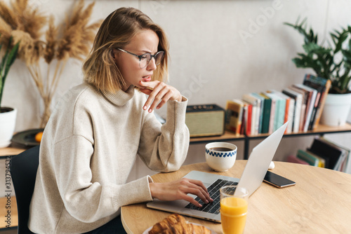 Tablou pe pânză Photo of perplexed woman using laptop while having breakfast