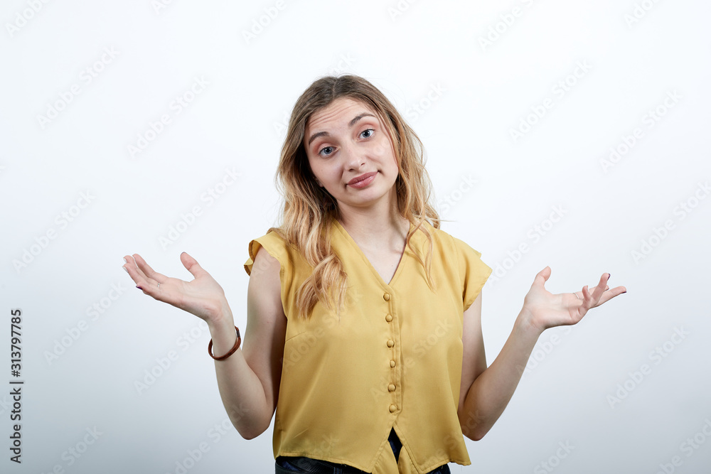 Disappointed woman spreads hand, looking at camera wearing fashion yellow shirt isolated on white background in studio. People sincere emotions, lifestyle concept. Disappointed woman spreads hand, looking at camera wearing fashion yellow shirt isolated on white background in studio. People sincere emotions, lifestyle concept.