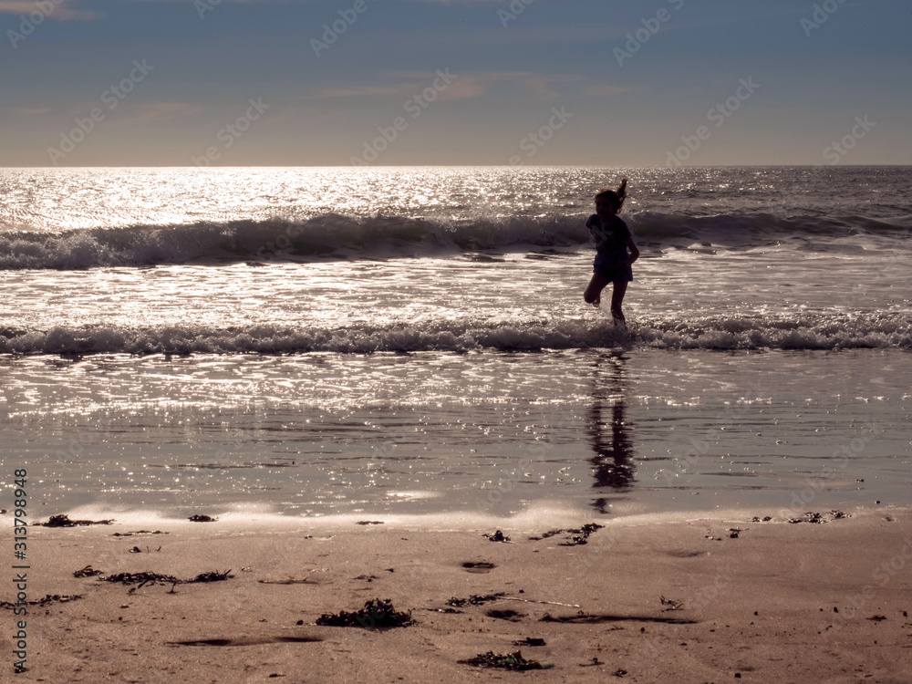 Young teenager girl silhouette running at ocean water. Sandy beach and sky. Concept childhood, carefree, fun, outdoor.