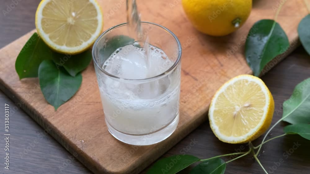 Man's hand pours lemon juice from pitcher into glass with ice on wooden board. Close up. Man's hand pours lemon juice from pitcher into glass with ice on wooden board. Close up.