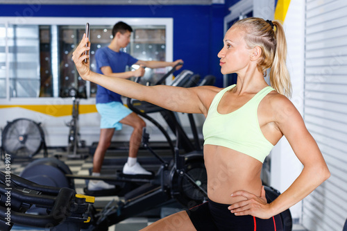Positive sporty girl taking selfie during workout at gym