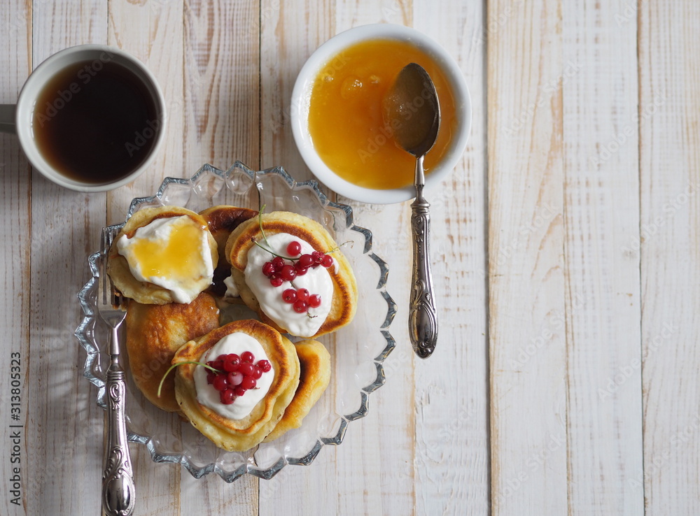 Fritters with sour cream and red currants. Therapeutic tea for colds with honey on a wooden white rustic table. Home kitchen. Fritters with sour cream and red currants. Therapeutic tea for colds with honey on a wooden white rustic table. Home kitchen.