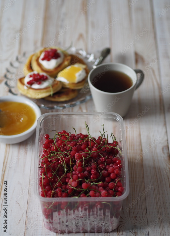 Fritters with sour cream and red currants. Therapeutic tea for colds with honey on a wooden white rustic table. Home kitchen. Fritters with sour cream and red currants. Therapeutic tea for colds with honey on a wooden white rustic table. Home kitchen.