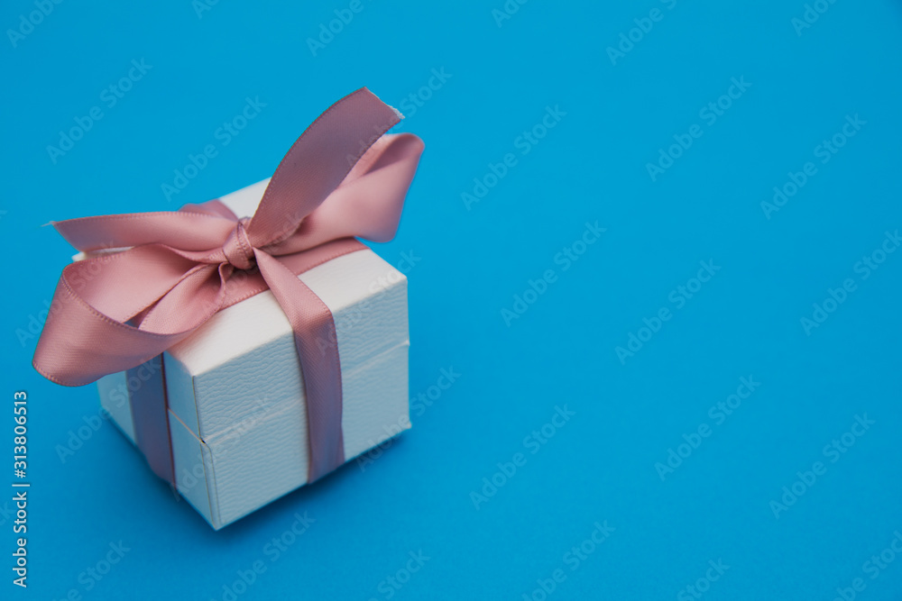 A gift box isolated over blue background with copy space. Box is tied with a ribbon. Valentine`s Day, 8 March, Mother and Women Day concept. Holidays gift or present A gift box isolated over blue background with copy space. Box is tied with a ribbon. Valentine`s Day, 8 March, Mother and Women Day concept. Holidays gift or present