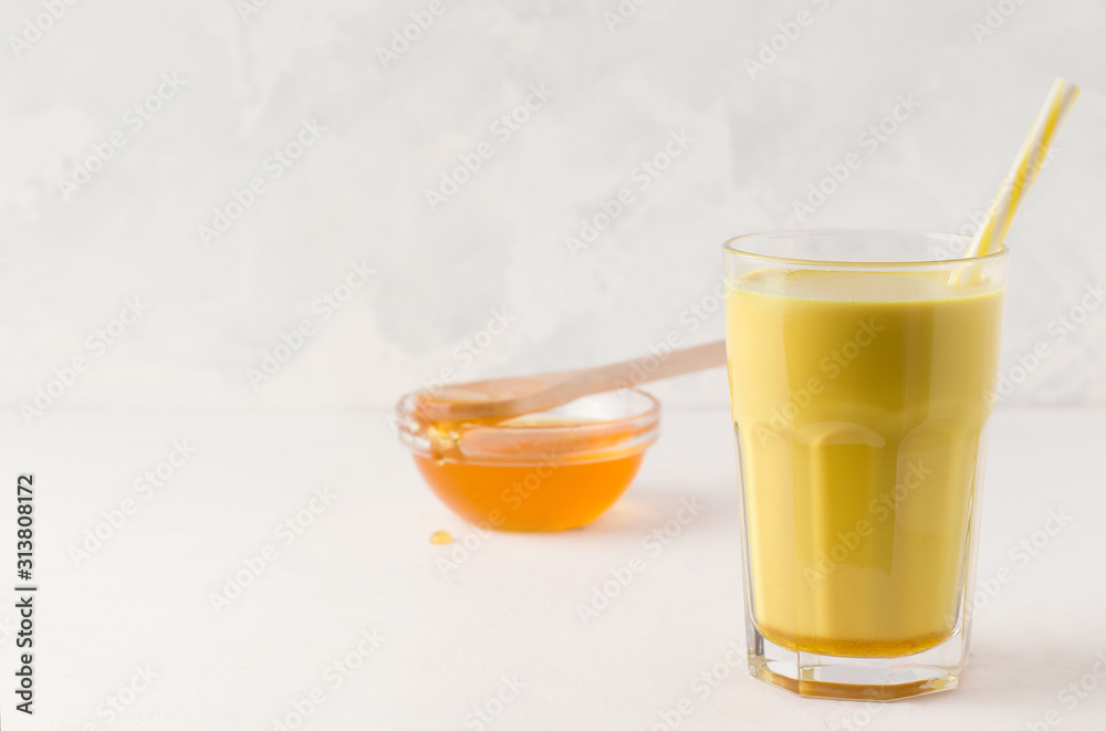 glass with golden milk on a light background next to a bowl with honey. There is a place for text glass with golden milk on a light background next to a bowl with honey. There is a place for text