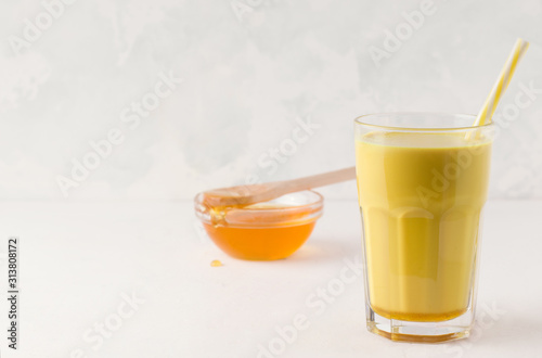 glass with golden milk on a light background next to a bowl with honey. There is a place for text photo