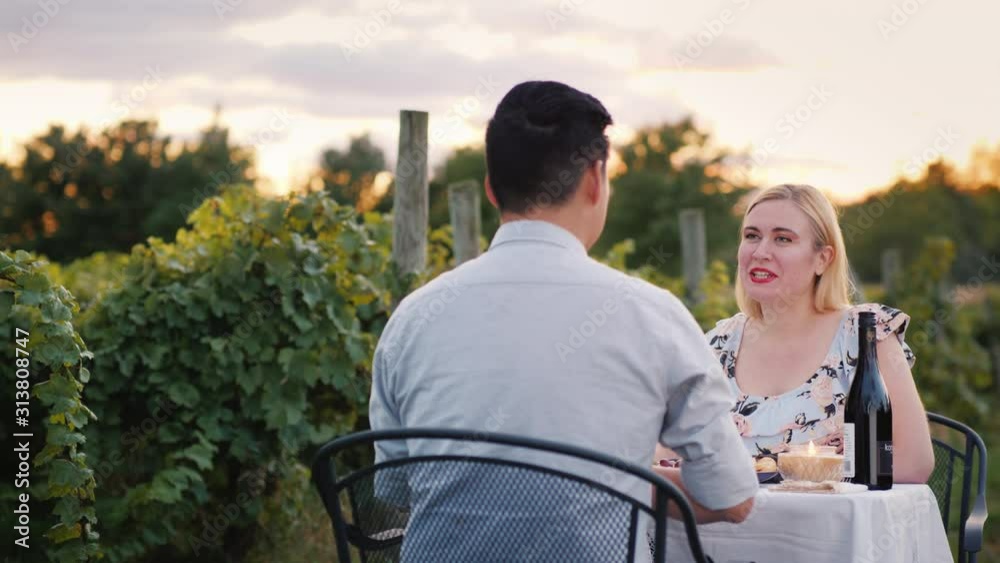 Young multi-ethnic couple has a romantic dinner in the vineyard with wine tasting Young multi-ethnic couple has a romantic dinner in the vineyard with wine tasting