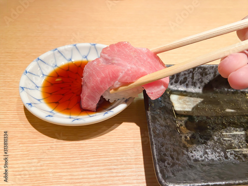 Close-up of super fatty tuna sushi is picked by a chopstick and being dipped into a source in a small bowl on wooden background.