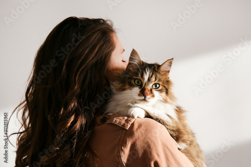 Portrait of young woman holding cute siberian cat with green eyes. Female hugging her cute long hair kitty. Background, copy space, close up. Adorable domestic pet concept.