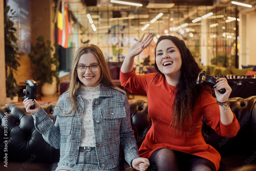Obraz premium Two girlfriends play video games, holding joysticks in their hands. Console games, addiction, streamers. The girls won the video game, give five, laugh. Female power, victory, joy.