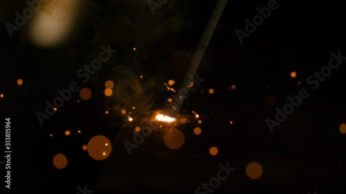 MACRO: Weld glows in the dark workshop as metalworker welds a piece of metal.