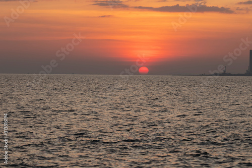 Fototapeta Naklejka Na Ścianę i Meble -  The red sun over the evening sea near the industrial area by the sea