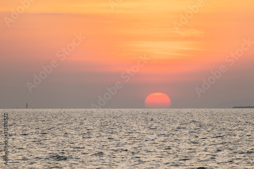 Fototapeta Naklejka Na Ścianę i Meble -  The red sun over the evening sea near the industrial area by the sea