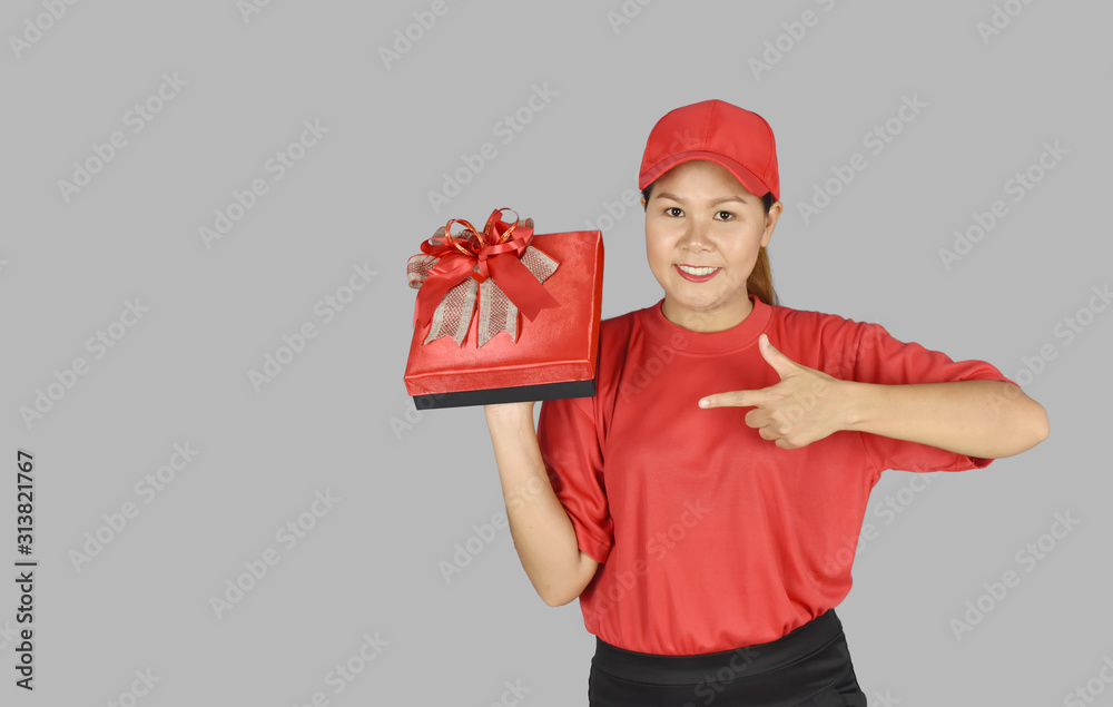delivery woman in red uniform holding present red gift box package on grey background. delivery woman in red uniform holding present red gift box package on grey background.