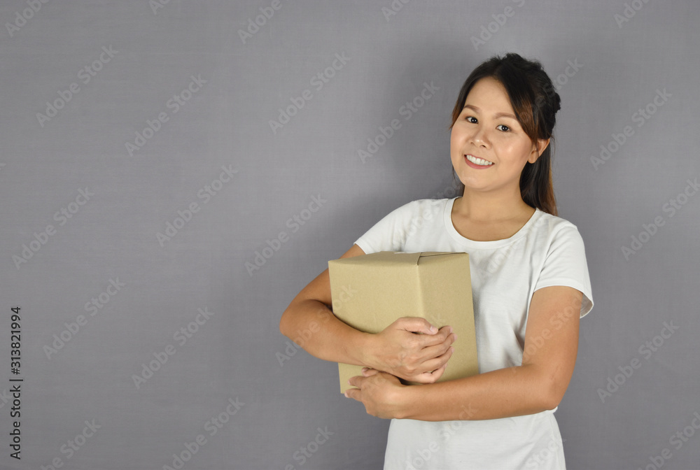 Asian woman smiling holding package box on grey background. Asian woman smiling holding package box on grey background.